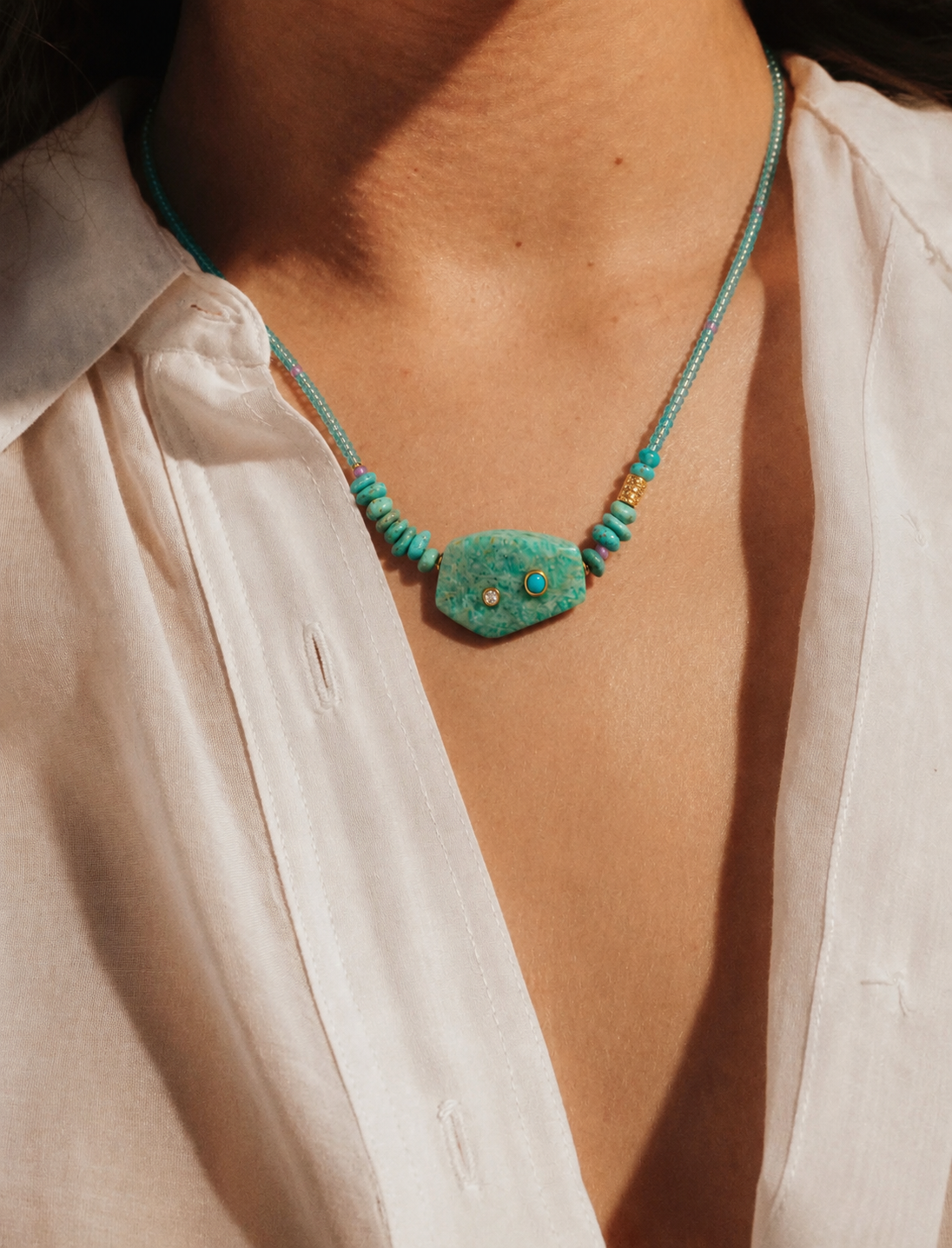 Model wearing the Azara focal necklace featuring an amazonite centerpiece with turquoise and moissanite accents, apatite bead strand, ruby details, and gold-plated findings.